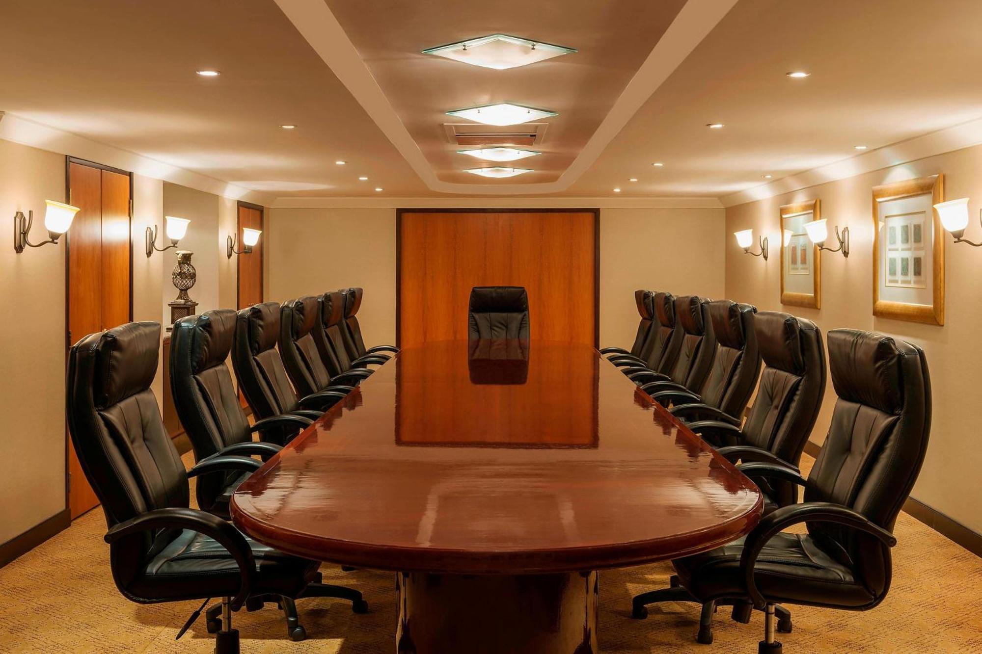 Sheraton Abu Dhabi Hotel & Resort Exterior photo The photo displays a large, elegant boardroom. In the center, there is a long, polished wooden table surrounded by black leather executive chairs. The room features soft lighting, with ceiling lights and wall sconces providing illumination. At the fa