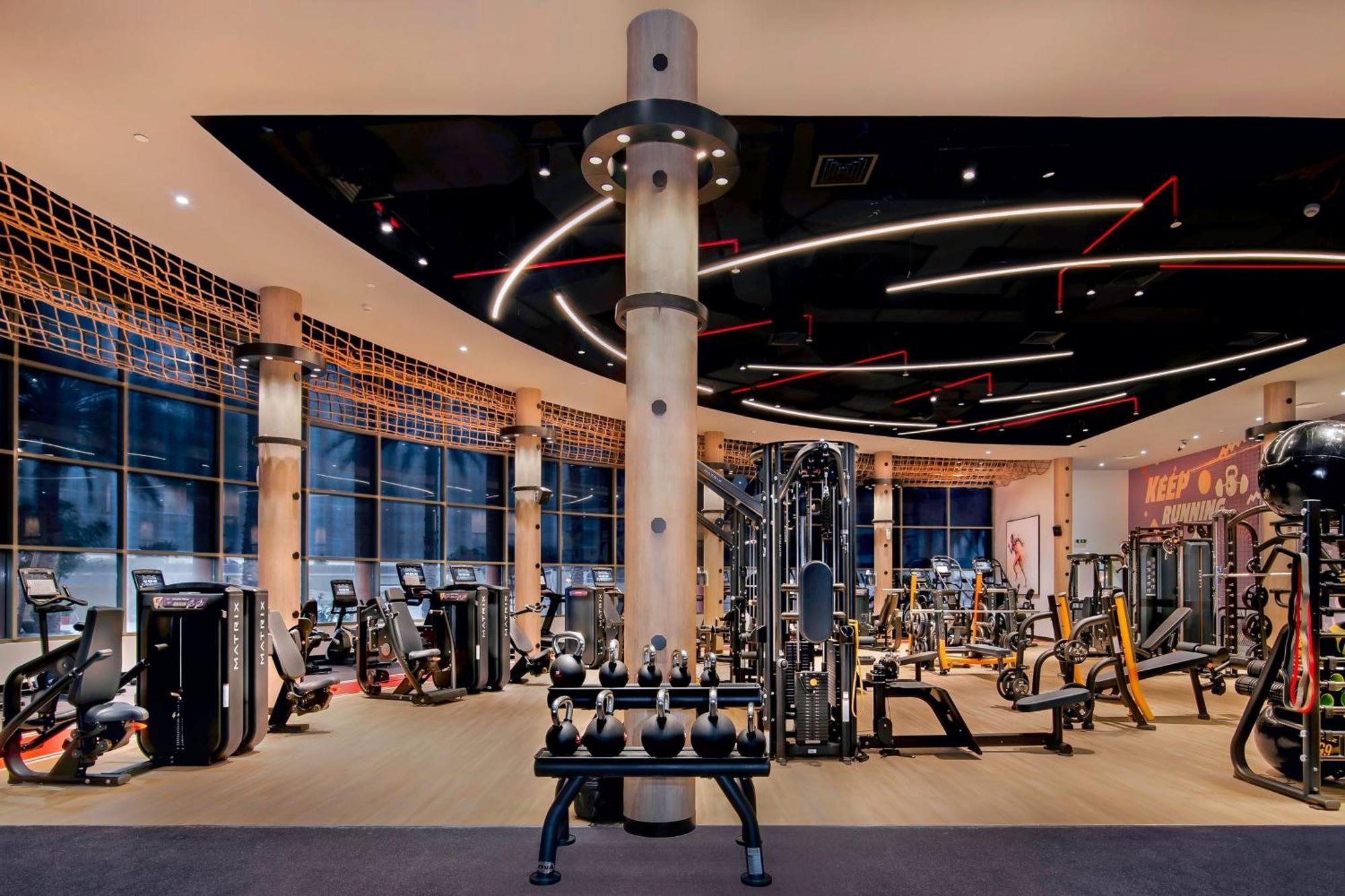 Sheraton Abu Dhabi Hotel & Resort Exterior photo The photo shows a modern gym interior featuring various fitness equipment. There are multiple workout stations, including weight machines and free weights like dumbbells. The design includes large windows that allow natural light to flood the space, 